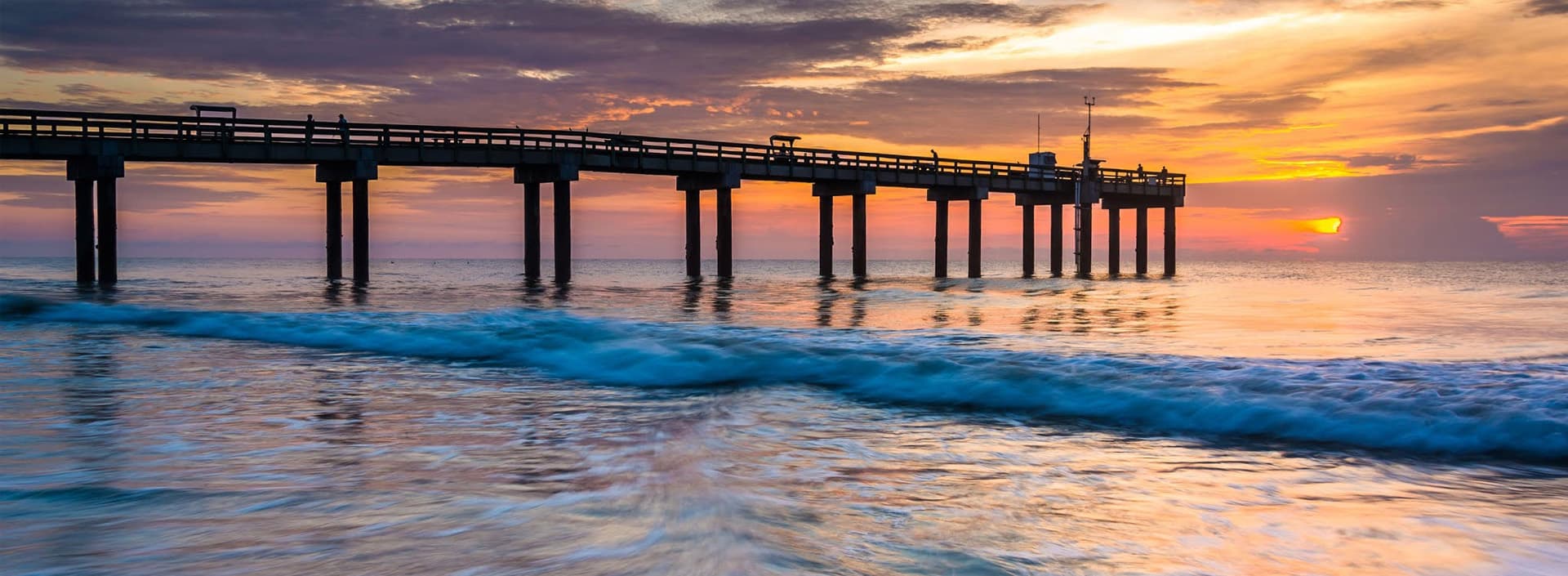 Sunset over a pier extending into calm ocean waters.