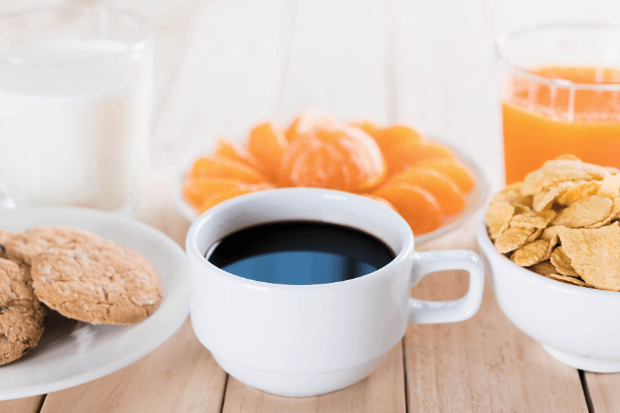 A breakfast spread featuring coffee, milk, cereal, cookies, orange slices, and orange juice.