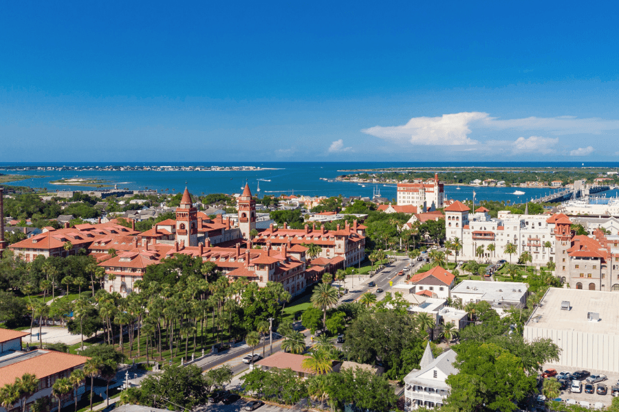 Aerial view of a coastal city featuring historic buildings and palm trees under a clear blue sky.